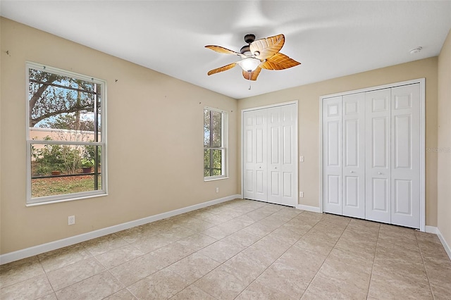 unfurnished bedroom featuring multiple windows, ceiling fan, light tile patterned flooring, and multiple closets