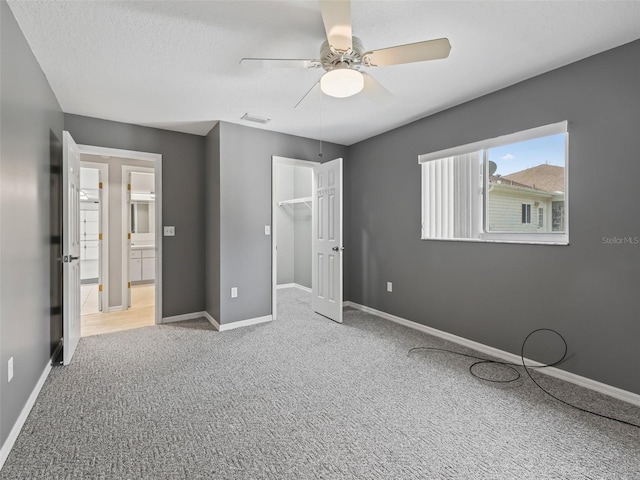 unfurnished bedroom with a closet, a spacious closet, a textured ceiling, carpet flooring, and ceiling fan