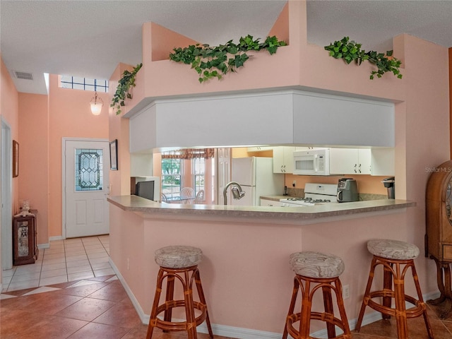 kitchen with kitchen peninsula, white appliances, a breakfast bar, and white cabinets