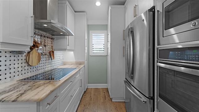 kitchen featuring backsplash, white cabinetry, appliances with stainless steel finishes, wall chimney exhaust hood, and light hardwood / wood-style flooring