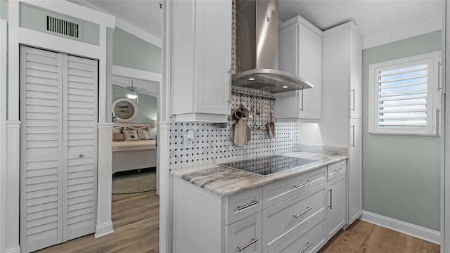 kitchen featuring backsplash, white cabinetry, light hardwood / wood-style floors, black electric cooktop, and wall chimney exhaust hood