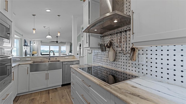 kitchen featuring white cabinetry, wall chimney range hood, appliances with stainless steel finishes, decorative backsplash, and light hardwood / wood-style floors