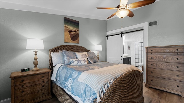 bedroom featuring a barn door, ensuite bathroom, ceiling fan, and wood-type flooring