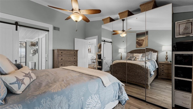 bedroom featuring light hardwood / wood-style flooring, a barn door, and ceiling fan