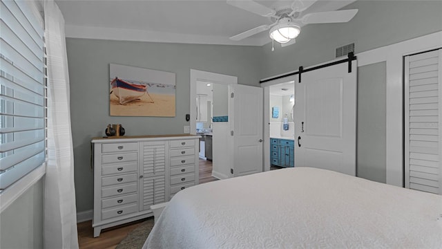 bedroom featuring ensuite bath, vaulted ceiling, a barn door, ceiling fan, and dark hardwood / wood-style floors