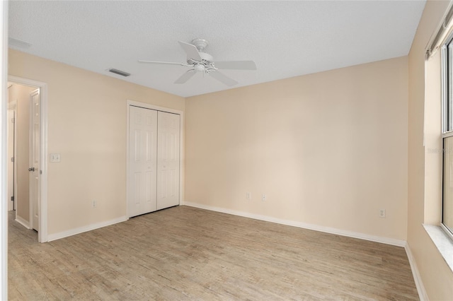 unfurnished bedroom with a closet, light wood-type flooring, a textured ceiling, and ceiling fan