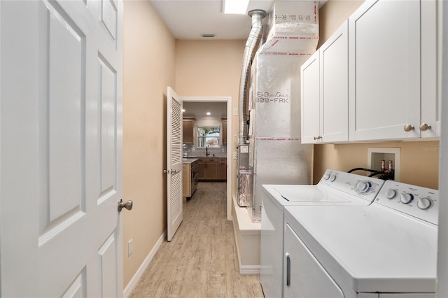 clothes washing area with cabinets, light hardwood / wood-style floors, separate washer and dryer, and sink