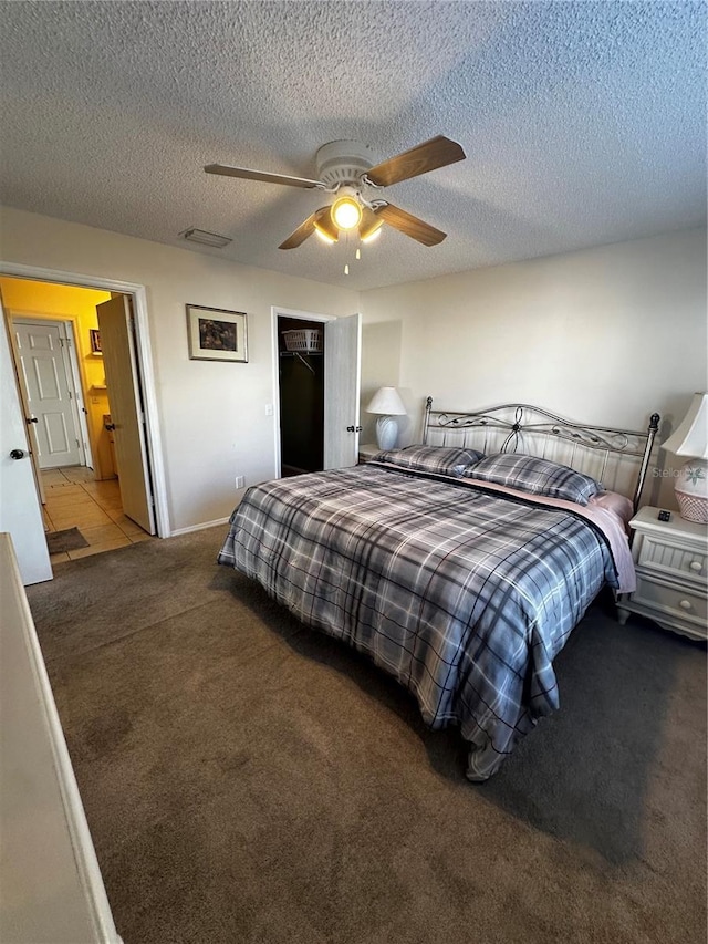 carpeted bedroom with a walk in closet, ceiling fan, a closet, and a textured ceiling