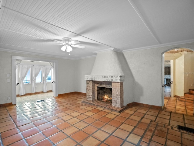 unfurnished living room with tile patterned flooring, a brick fireplace, ceiling fan, and crown molding