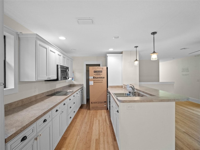 kitchen featuring stainless steel appliances, sink, light hardwood / wood-style flooring, white cabinetry, and hanging light fixtures