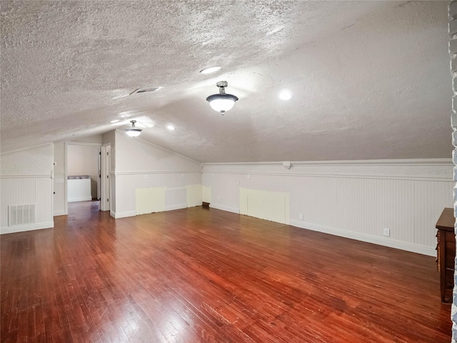 additional living space featuring hardwood / wood-style flooring, lofted ceiling, and a textured ceiling