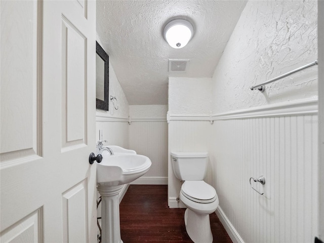 bathroom featuring hardwood / wood-style flooring, wood walls, toilet, and a textured ceiling