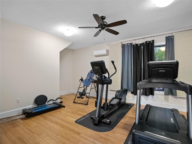 exercise area featuring ceiling fan, hardwood / wood-style floors, a wall mounted air conditioner, and a textured ceiling