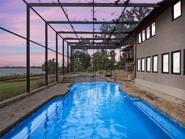 pool at dusk with an in ground hot tub, a water view, glass enclosure, and a patio area