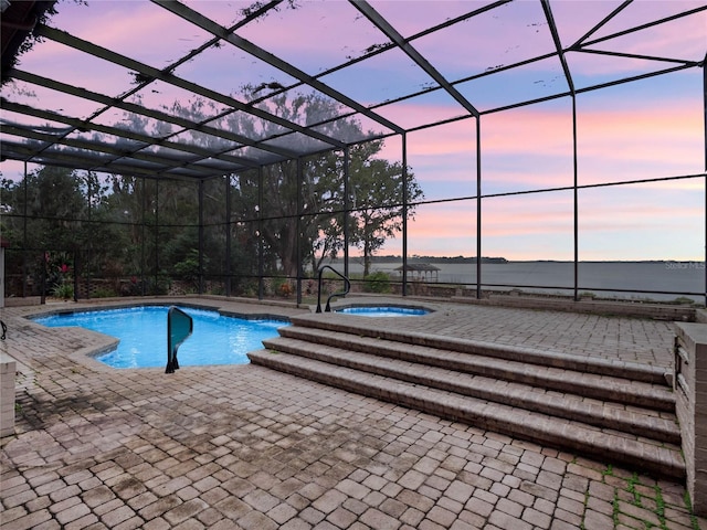 pool at dusk featuring glass enclosure, a patio area, and a jacuzzi