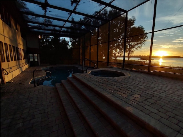 pool at dusk featuring an in ground hot tub, a patio, a water view, and a lanai