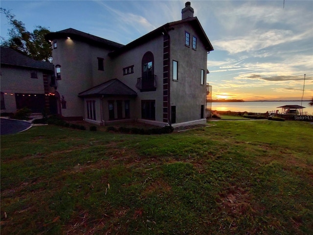 back house at dusk featuring a yard and a water view