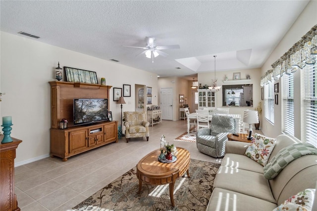 living room featuring a textured ceiling, light tile patterned flooring, and ceiling fan with notable chandelier