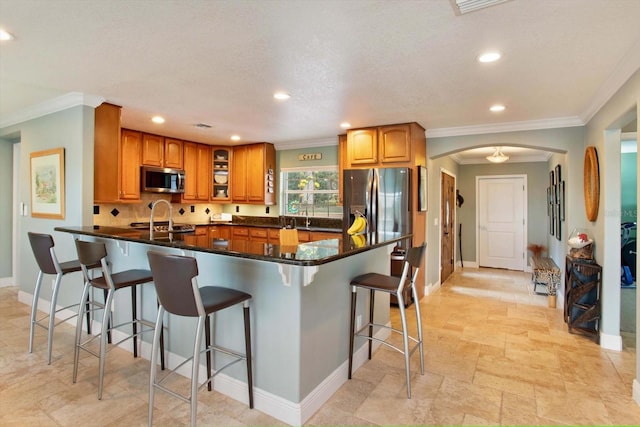 kitchen with kitchen peninsula, crown molding, dark stone counters, a breakfast bar, and appliances with stainless steel finishes