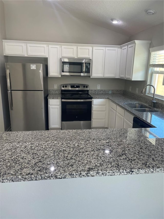 kitchen with sink, white cabinets, vaulted ceiling, and appliances with stainless steel finishes