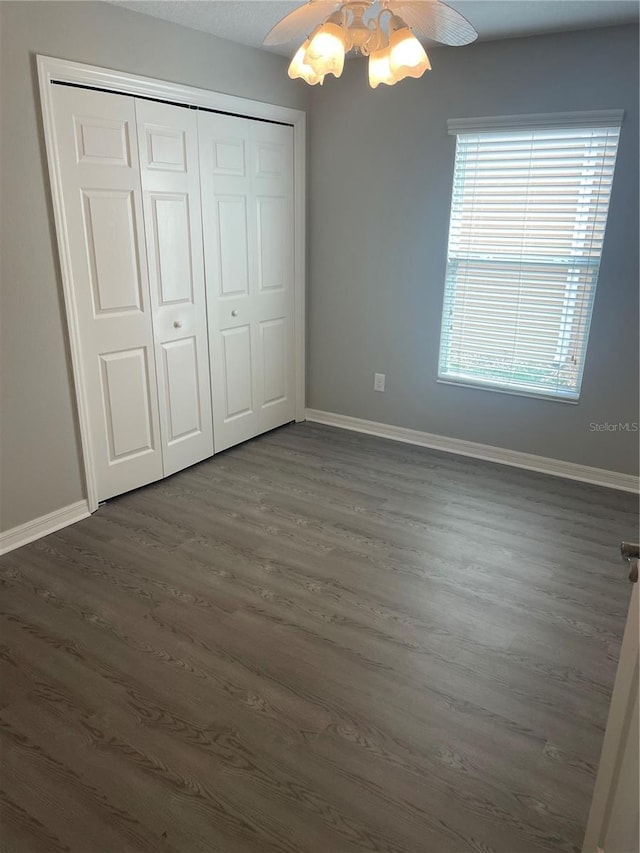 unfurnished bedroom featuring a ceiling fan, a closet, dark wood finished floors, and baseboards