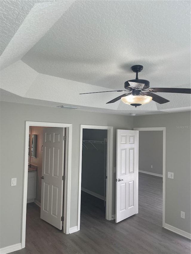 unfurnished bedroom featuring a walk in closet, baseboards, dark wood finished floors, and a closet