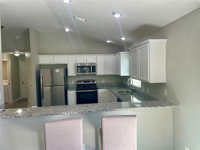 kitchen featuring lofted ceiling, appliances with stainless steel finishes, light stone counters, a peninsula, and white cabinetry