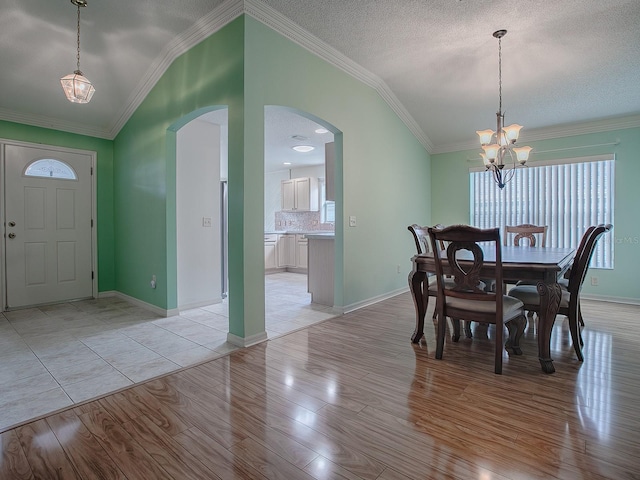 dining room with lofted ceiling, a notable chandelier, a textured ceiling, ornamental molding, and light wood-type flooring