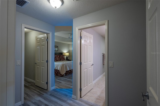 corridor featuring a textured ceiling, light wood finished floors, visible vents, and baseboards