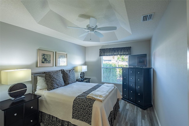 bedroom with a raised ceiling, visible vents, a textured ceiling, wood finished floors, and baseboards