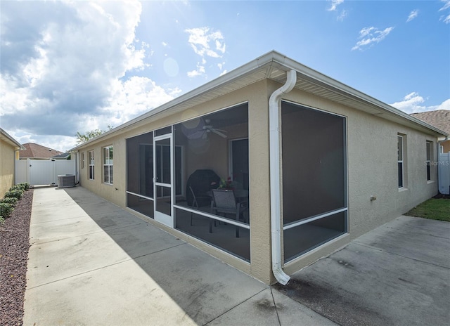 view of side of property with a sunroom, a gate, fence, central air condition unit, and stucco siding