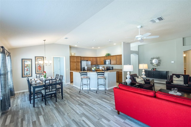 living area with baseboards, visible vents, vaulted ceiling, light wood-style floors, and ceiling fan with notable chandelier