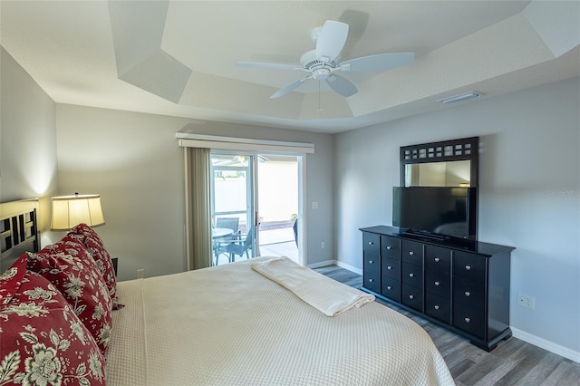 bedroom with wood finished floors, visible vents, baseboards, access to exterior, and a raised ceiling