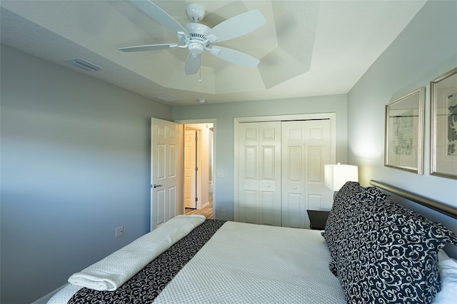 bedroom with visible vents, a tray ceiling, ceiling fan, and a closet