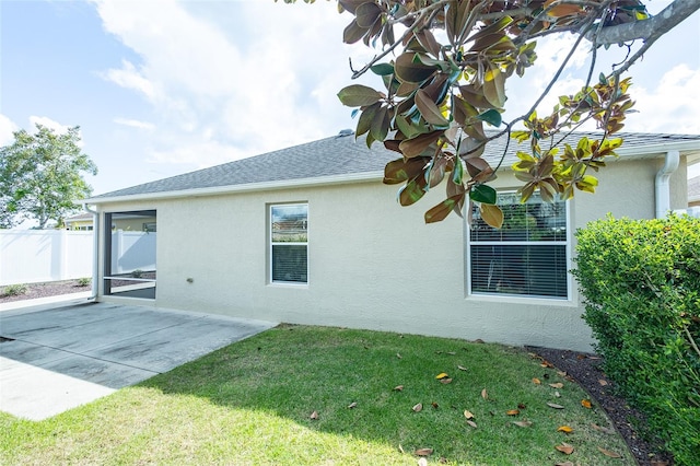 view of property exterior with roof with shingles, a yard, a patio, stucco siding, and fence