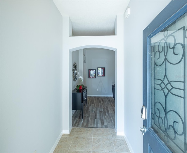 foyer with arched walkways, light tile patterned flooring, and baseboards