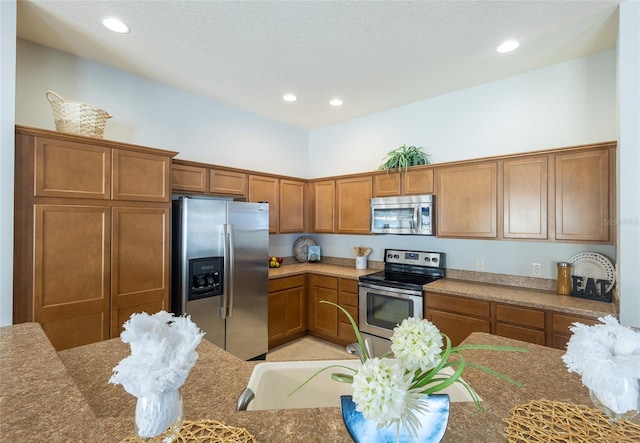 kitchen with brown cabinets, stainless steel appliances, a textured ceiling, stone counters, and recessed lighting