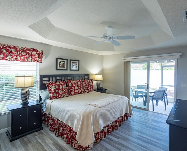 bedroom with visible vents, wood finished floors, access to exterior, a tray ceiling, and a textured ceiling