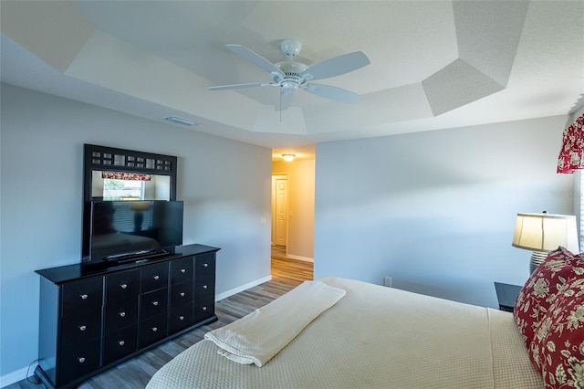 bedroom featuring a ceiling fan, visible vents, baseboards, dark wood-style floors, and a raised ceiling