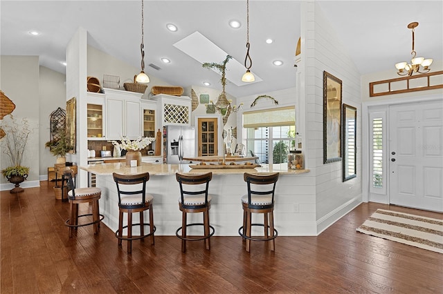 kitchen with dark hardwood / wood-style floors, a breakfast bar area, decorative light fixtures, white cabinets, and stainless steel fridge with ice dispenser