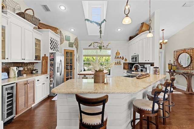 kitchen with stainless steel appliances, beverage cooler, a kitchen island with sink, white cabinets, and pendant lighting