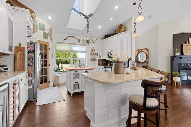 kitchen featuring dark wood-type flooring, a center island, white cabinets, hanging light fixtures, and a breakfast bar