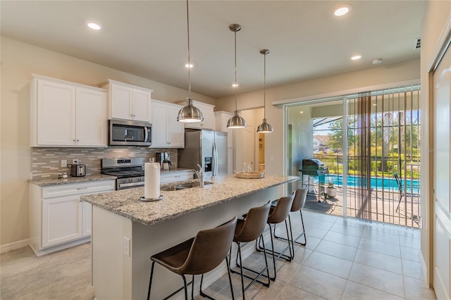 kitchen featuring a center island with sink, appliances with stainless steel finishes, hanging light fixtures, white cabinets, and decorative backsplash