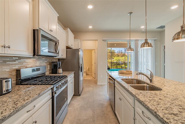 kitchen with light stone counters, stainless steel appliances, decorative backsplash, sink, and white cabinets