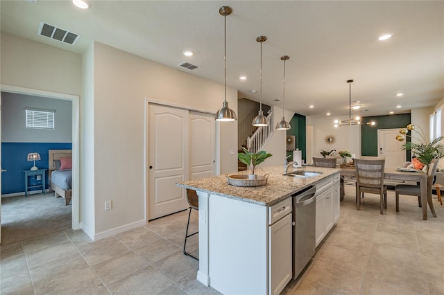 kitchen with a center island with sink, white cabinetry, light stone countertops, pendant lighting, and sink