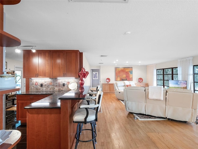 kitchen featuring decorative backsplash, light hardwood / wood-style flooring, kitchen peninsula, and a breakfast bar area