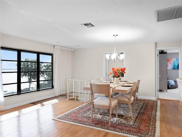 dining space with light hardwood / wood-style flooring, a textured ceiling, and an inviting chandelier