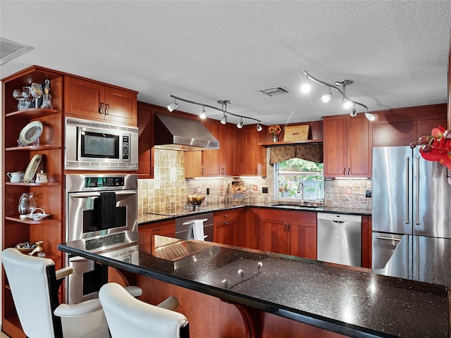 kitchen with stainless steel appliances, a textured ceiling, a kitchen bar, sink, and wall chimney exhaust hood