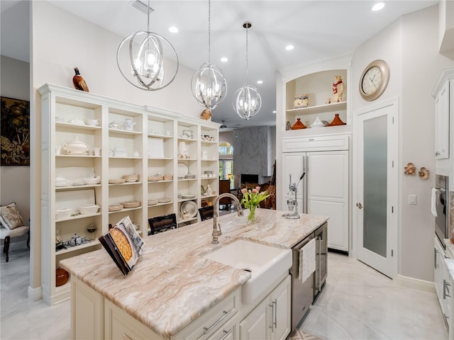 kitchen with a center island with sink, sink, hanging light fixtures, light stone counters, and a chandelier