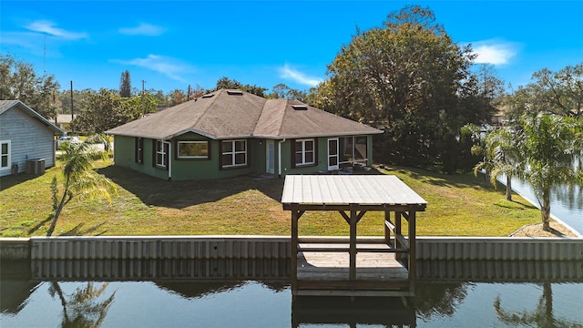 back of house with a yard, stucco siding, a shingled roof, a water view, and central AC